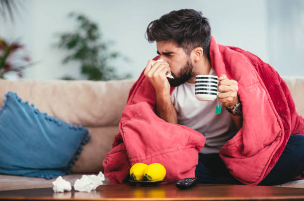 man blowing his nose while lying sick in bed - cold imagens e fotografias de stock