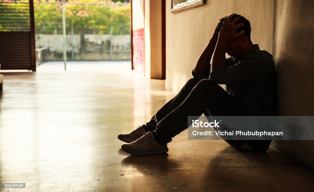 Emotional moment: man sitting holding head in hands, stressed sad young male having mental problems, feeling bad, depressed, disappointed, hopeless. Desperate man in the dark corner needing help. Teenager Stock Photo