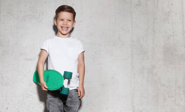 niño patinador en camiseta blanca, muro de hormigón en el fondo - t shirt child white portrait fotografías e imágenes de stock