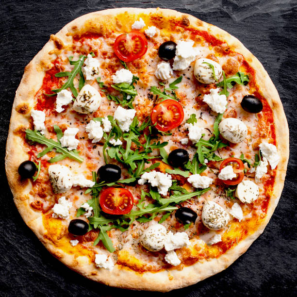 Vegetarian pizza in a pan, with mozzarella, onion, garlic, zucchini, cherry tomato, cottage cheese and salad rocket. Top view.