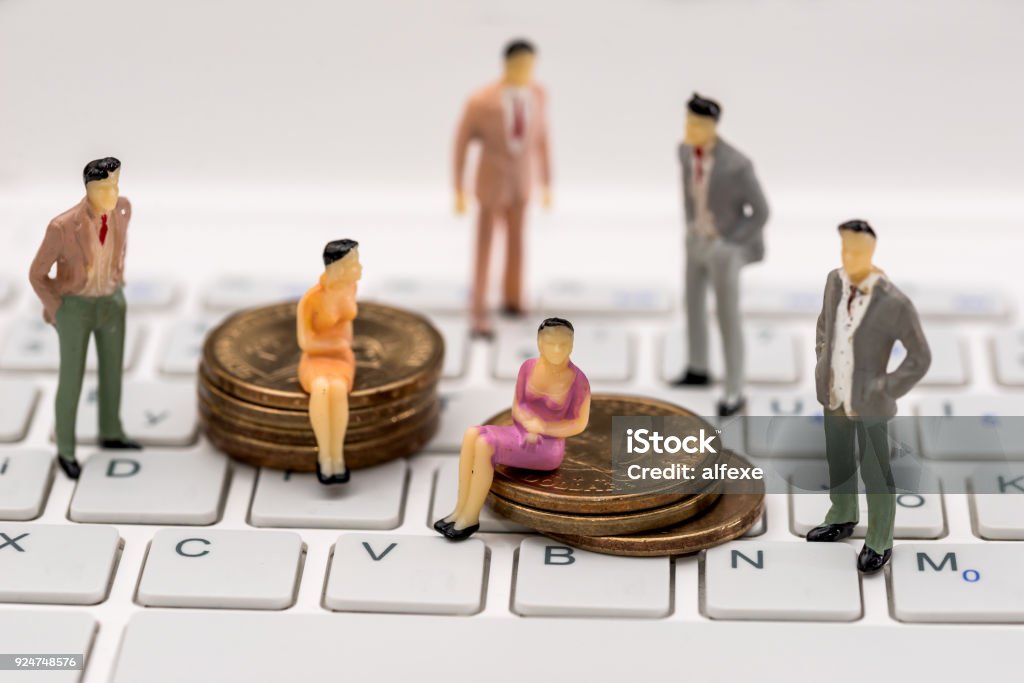 Small toy people are standing on a laptop and sitting on coins . Figurine Stock Photo