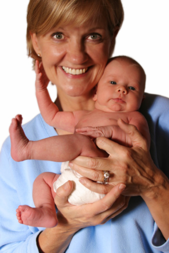 Mother holding sleeping newborn baby looking at the camera smiling