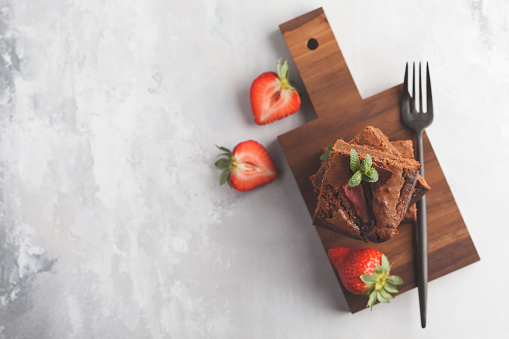 A stack of pieces of homemade dark chocolate brownie with strawberries on a wooden board. Top view, copy space.