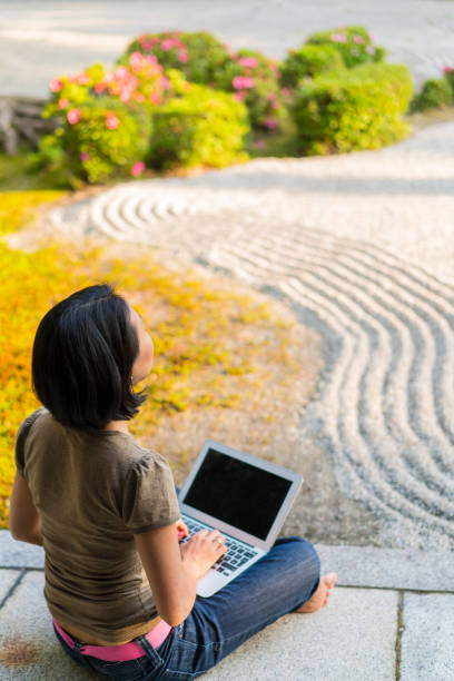 vue latérale d’une femme assise sur le podium du temple, taper sur un ordinateur portable tout en appréciant le zen jardin de chion-ji à kyoto, japon - zen like women temple meditating photos et images de collection