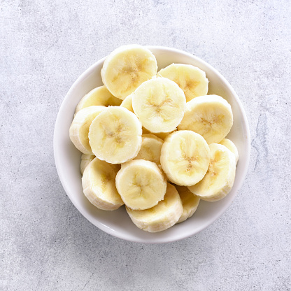 Banana slices in bowl over stone background with copy space. Healthy natural vitamin snack. Top view, flat lay