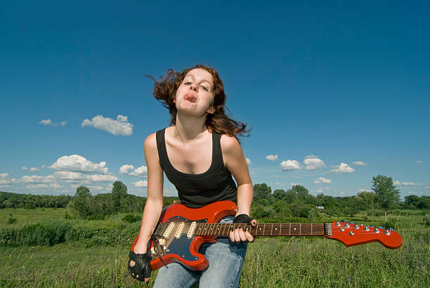Sitting young woman with guitar in countryside. Processed image with soft increase of saturation and added vignette.