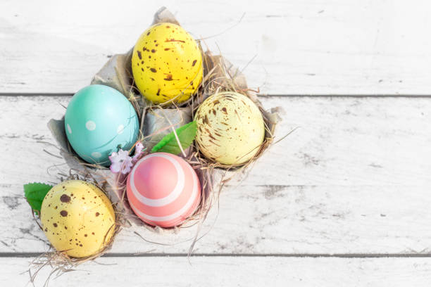 istock Easter eggs in egg cartoon box on white rustic wooden background close up. Festive decorations. Happy Easter!