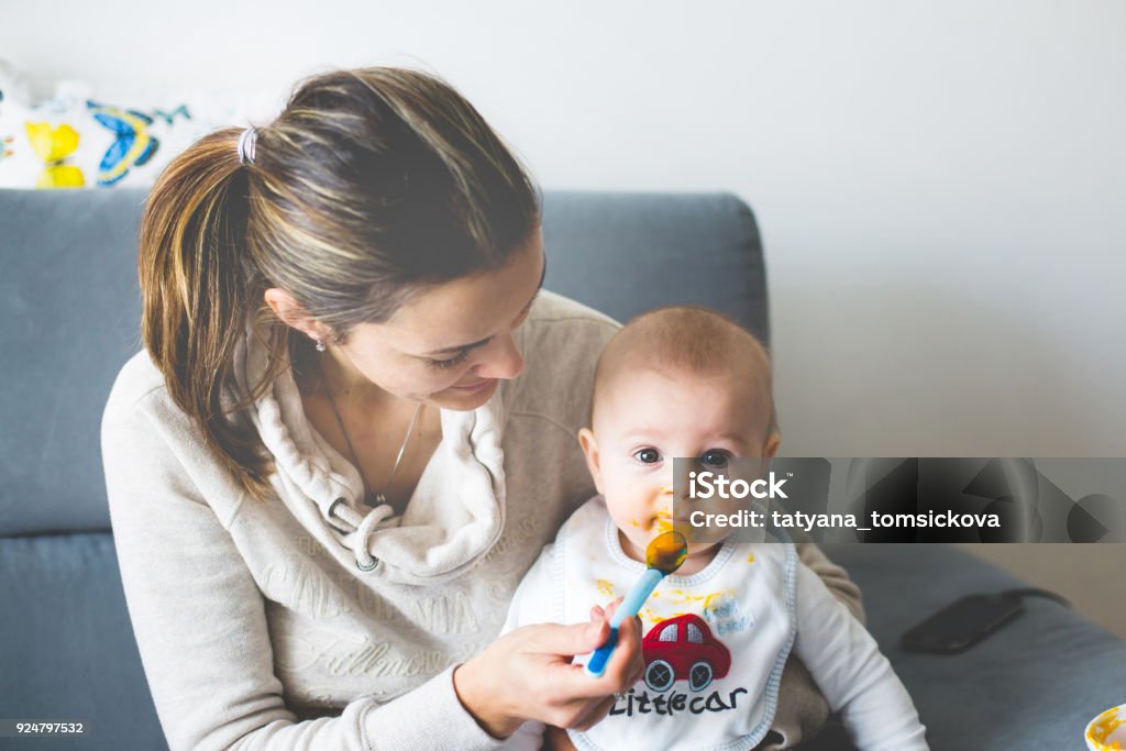 Mother, feeding her baby boy with mashed pumpking Mother, feeding her baby boy with mashed pumpking for the first time Adult Stock Photo