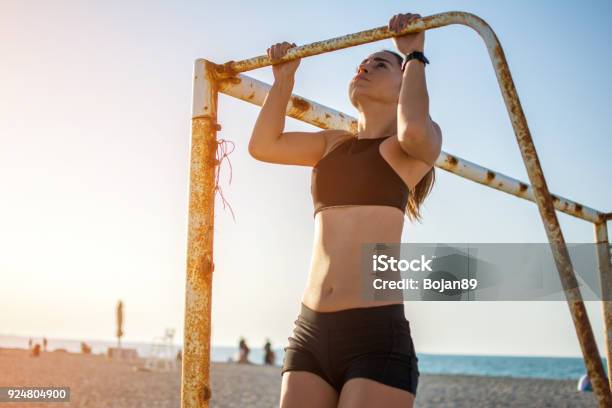 Sporty Fit Young Woman Doing Pull Ups On Metal Goal Frame On Sandy Beach During Sunset Stock Photo - Download Image Now