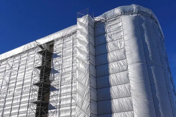 House building, construction, restoration or maintenance site with scaffolding and protective covering of gray tarpaulin