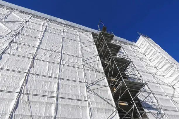House building, construction, restoration or maintenance site with scaffolding and protective covering of gray tarpaulin