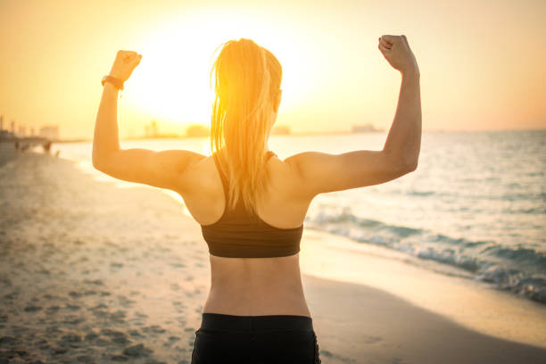 rückansicht des starken sportliches girl zeigt muskeln am strand bei sonnenuntergang. - beach body stock-fotos und bilder