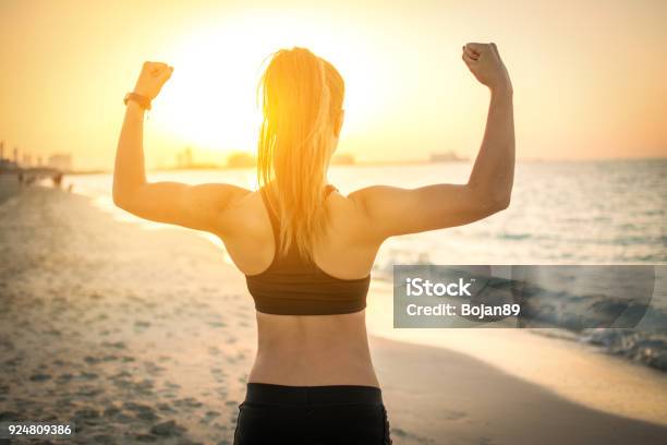 Photo libre de droit de Vue Arrière Du Forte Fille Sportive Montrant Les Muscles À La Plage Pendant Le Coucher Du Soleil banque d'images et plus d'images libres de droit de Plage