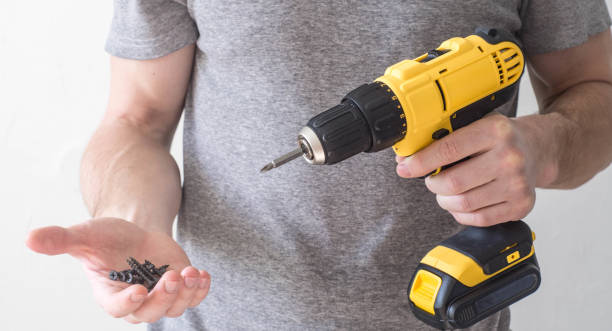 ручной электрооборукладчик: желтая электрическая отвертка в руках человека и винт в ладони - holding screwdriver стоковые фото и изображения