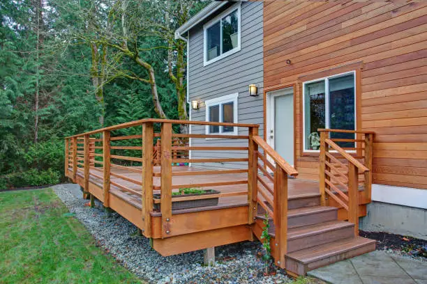 Charming newly renovated home exterior, natural wood siding and grey siding create a beautiful curb appeal. Detail view of a nice walk out deck with wooden handrails.
