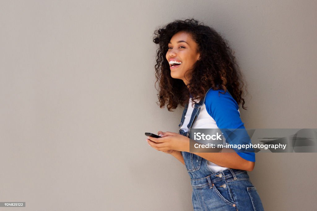happy young african woman laughing with cellphone Side portrait of happy young african woman laughing with cellphone One Woman Only Stock Photo