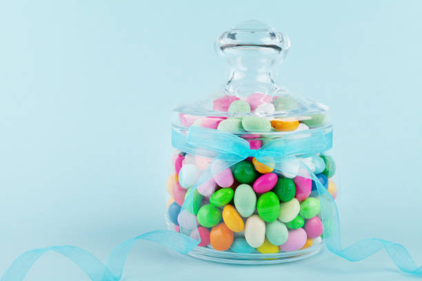 glass jar stuffed with colorful candy against blue background. gifts for birthday or happy easter. - flavored ice variation birthday candy imagens e fotografias de stock