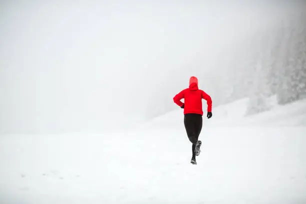 Trail running woman in winter mountains. Sport, fitness inspiration and motivation. Young happy woman cross country running in mountains on snow, winter day. Female trail runner jogging outdoors.