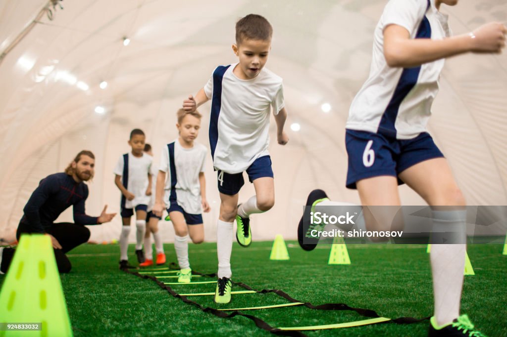 Boys training Row of boys running on green football field during training with instructor Child Stock Photo