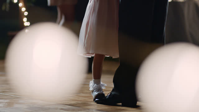 SLO MO. Young girl stands on her father's feet on dance floor at wedding reception.
