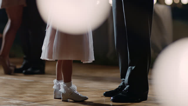 SLO MO. Young girl dances with her dad under twinkling lights at wedding reception.
