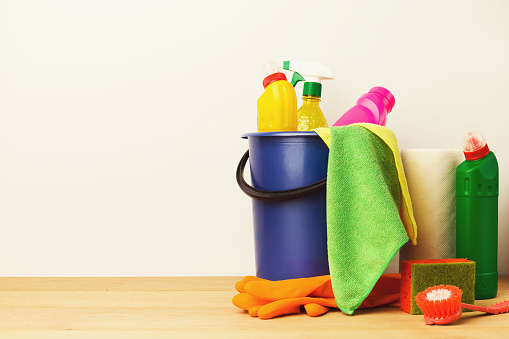 Variety of house cleaning products on wood table at white background, closeup. Bucket, brush, rubber gloves, disinfection items. Tidying up, spring-cleaning concept, copy space