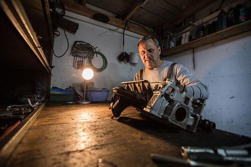 Senior man working at his workshop holding vehicle engine