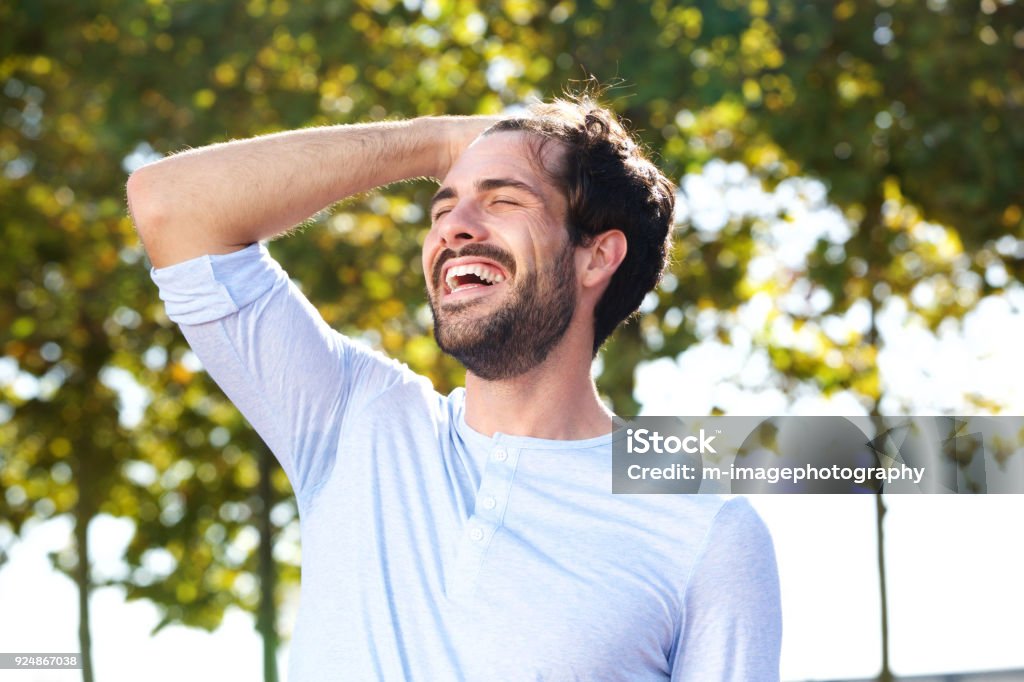 happy young man smiling outdoors with hand in hair Portrait of happy young man smiling outdoors with hand in hair Hand In Hair Stock Photo