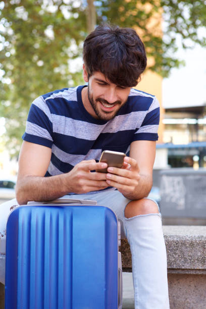 istock Young man sitting with suitcase looking at mobile phone 924867110