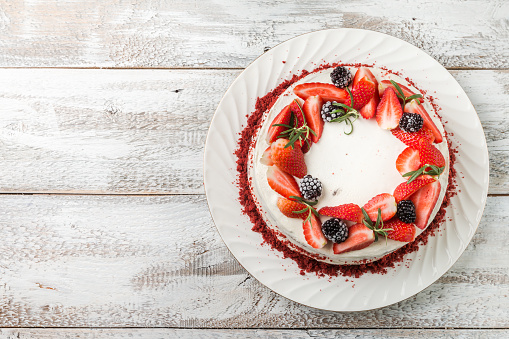 Homemade cake Red Velvet decorated with cream and berries over white wooden background, top view