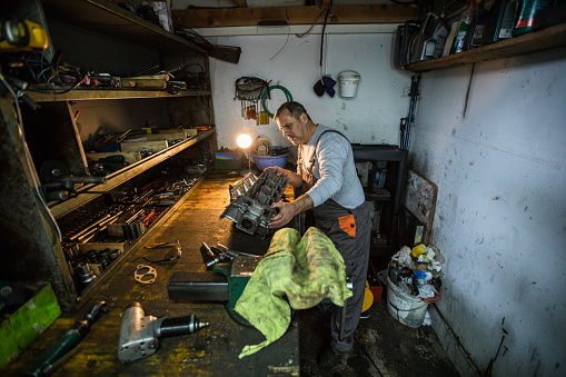 Senior man working at his workshop holding vehicle engine