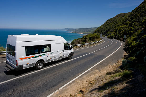A campervan tours along a windy road through the hills and by the ocean. The day is a clear and blue, ideal for touring. This image has lots of copy and cropping space.