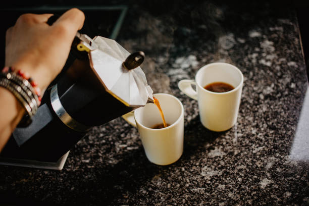 Preparing fresh coffee in moka pot on electric stove. Pouring hot steaming coffee into two white mugs. Preparing fresh coffee in moka pot on electric stove. Pouring hot steaming coffee into two white mugs. moka stock pictures, royalty-free photos & images