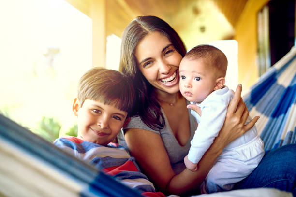 Portrait of a cheerful mother relaxing on a hammock with her two little boys outside at home during the day
