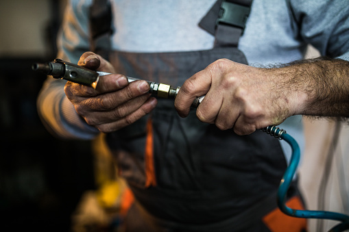 Close up of Senior man's hands  working at workshop ,holding air compressor hose