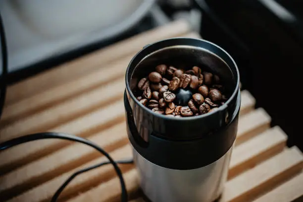 Preparing fresh coffee in moka pot on electric stove. Grinding roasted coffee beans in electric mill. Close up.