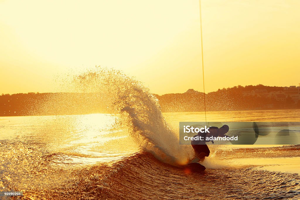 Wakeboarder slashes wake on heel side during sunset A wakeboarder slashes wake on his heel side on a lake in China during very late afternoon sunset making a large spray behind him. Wakeboarding Stock Photo