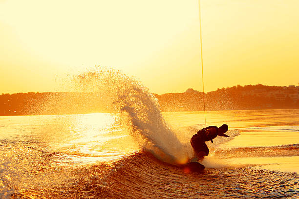 Wakeboarder slashes wake on heel side during sunset A wakeboarder slashes wake on his heel side on a lake in China during very late afternoon sunset making a large spray behind him. punting stock pictures, royalty-free photos & images