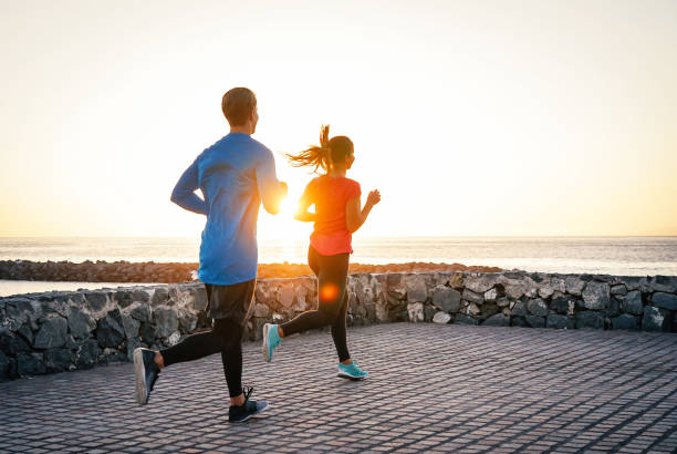 gesundheit junges paar zusammen joggen als nächstes der ozean bei einem herrlichen sonnenuntergang - menschen trainieren sie auf den strand - beziehung, sport, lifestyle-konzept - marathon sport sports training city street stock-fotos und bilder