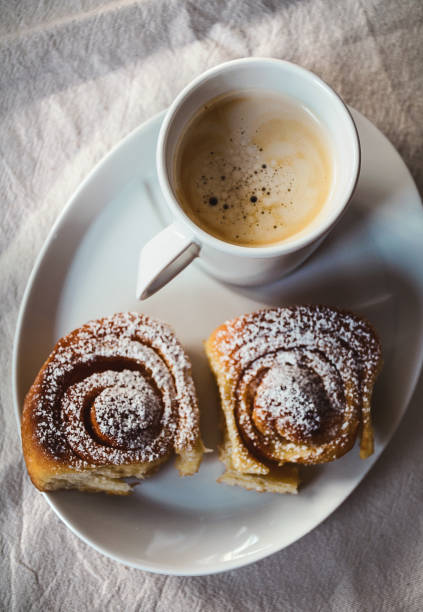 Cup of coffee with two cinnamon buns on white plate. View from above, white background.
