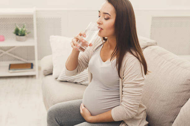 istock Pregnant woman drinking water sitting on sofa 924915880