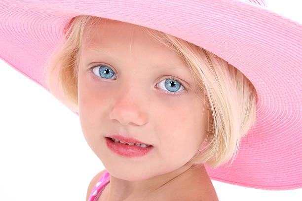 Beautiful blue-eyed baby sitting in the sunshine, outdoors  amongst desert vegetation while wearing purple hat