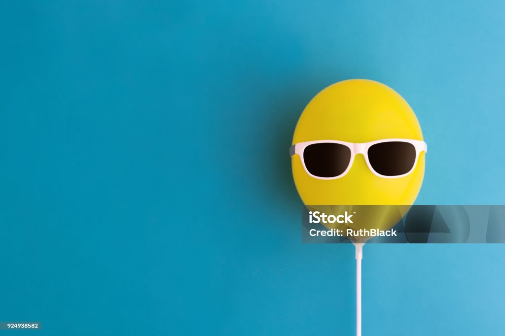 Yellow balloon with sunglasses Yellow party balloon with sunglasses on a blue background Offbeat Stock Photo