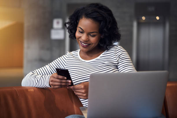 istock Smiling African student checking her phone and using a laptop 924943936