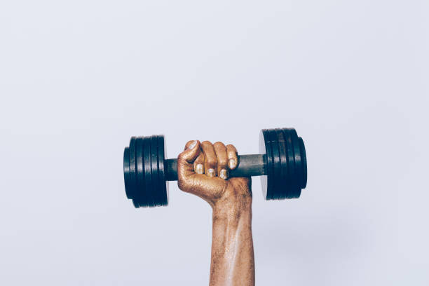 Female hand in golden glitter holds a dumbbell on a gray background close-up