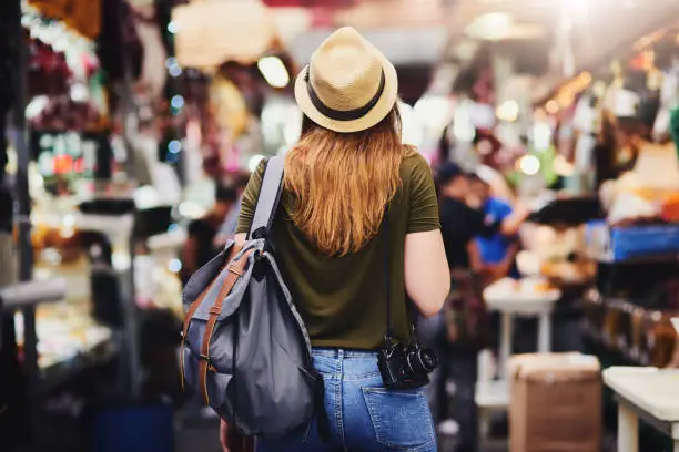 Rearview shot of an unrecognizable woman wearing a hat and walking through a busy market outside during the day