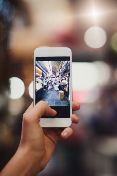 Showing everyone where I am and what I'm up to Shot of an unrecognizable person's hand holding a cellphone and taking photos of a busy market outside during the day ariel west bank stock pictures, royalty-free photos & images