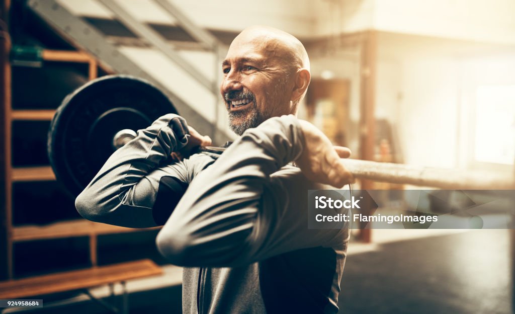 Homme d’âge mûr fit lever des poids et souriant dans une salle de sport - Photo de Exercice physique libre de droits