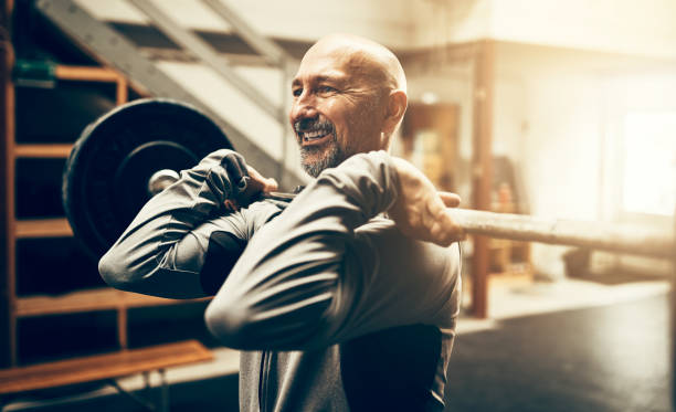 Fit mature man lifting weights and smiling in a gym stock photo