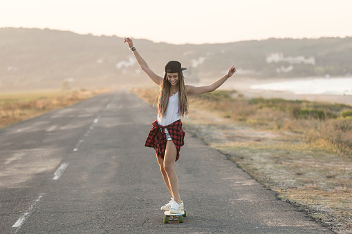 Beautifl young woman skateboarding on country road, at sunset.